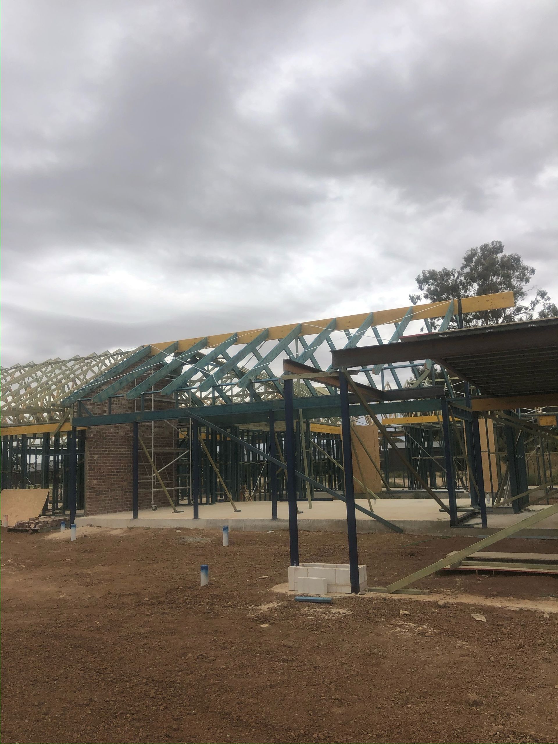 Construction site with wooden framing and a partially built roof, under an overcast sky.