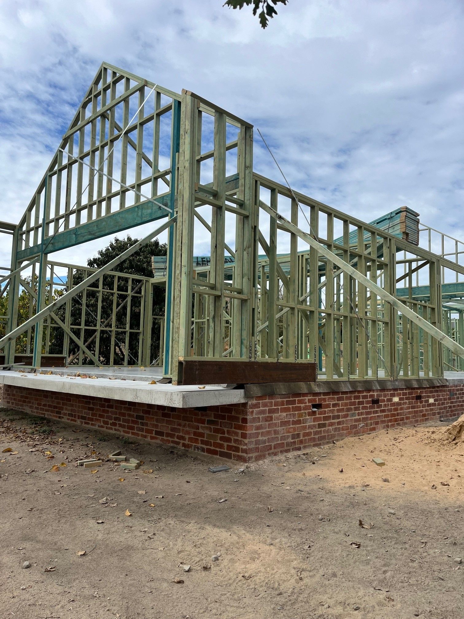Wooden frame of a house under construction on a brick foundation, against a cloudy sky.