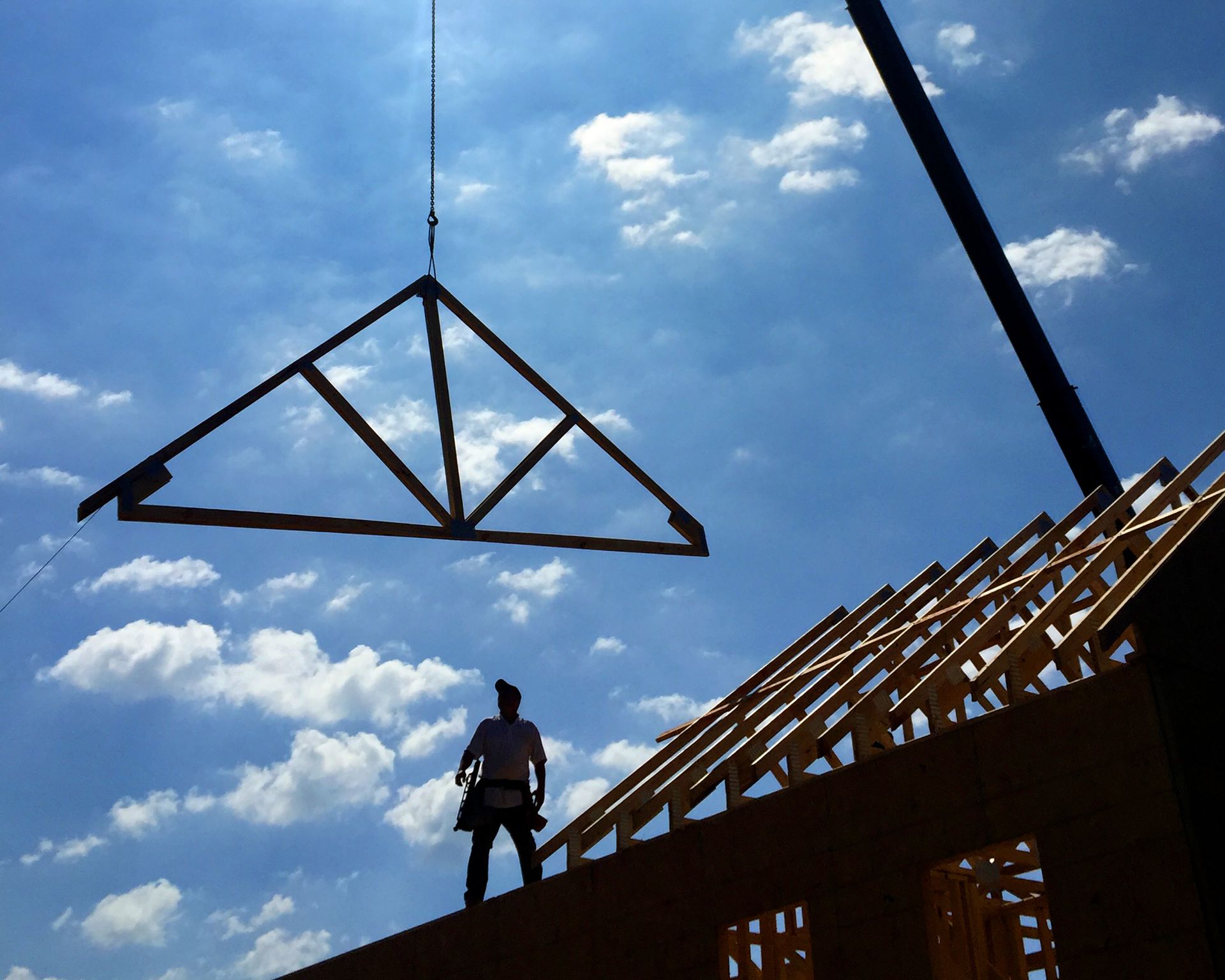 Construction worker placing a prefab roof truss onto a house under construction.