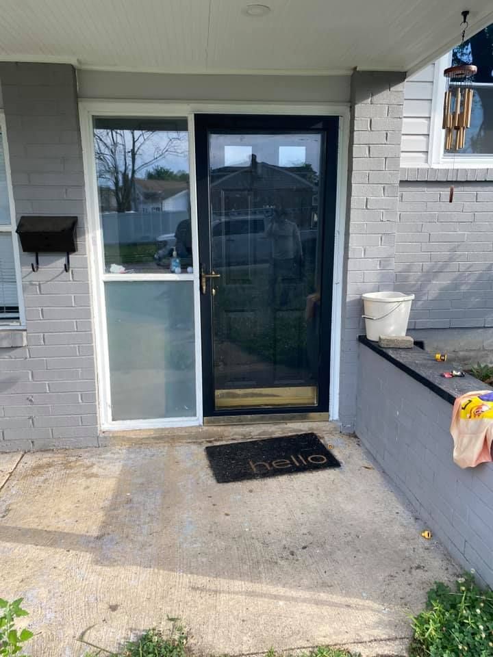 The front door of a brick house with a black door and a welcome mat.
