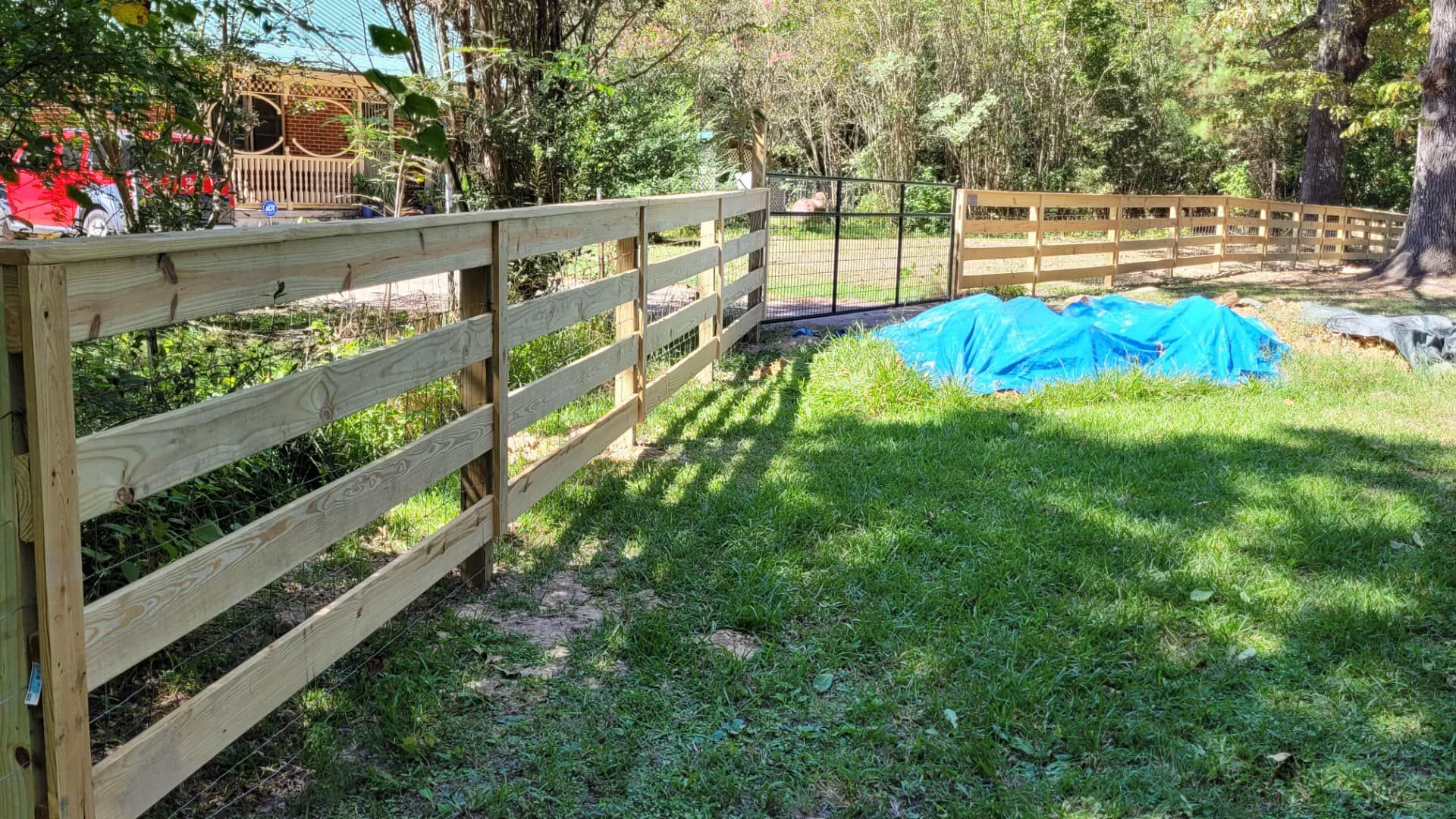 A wooden fence is in the middle of a lush green field.