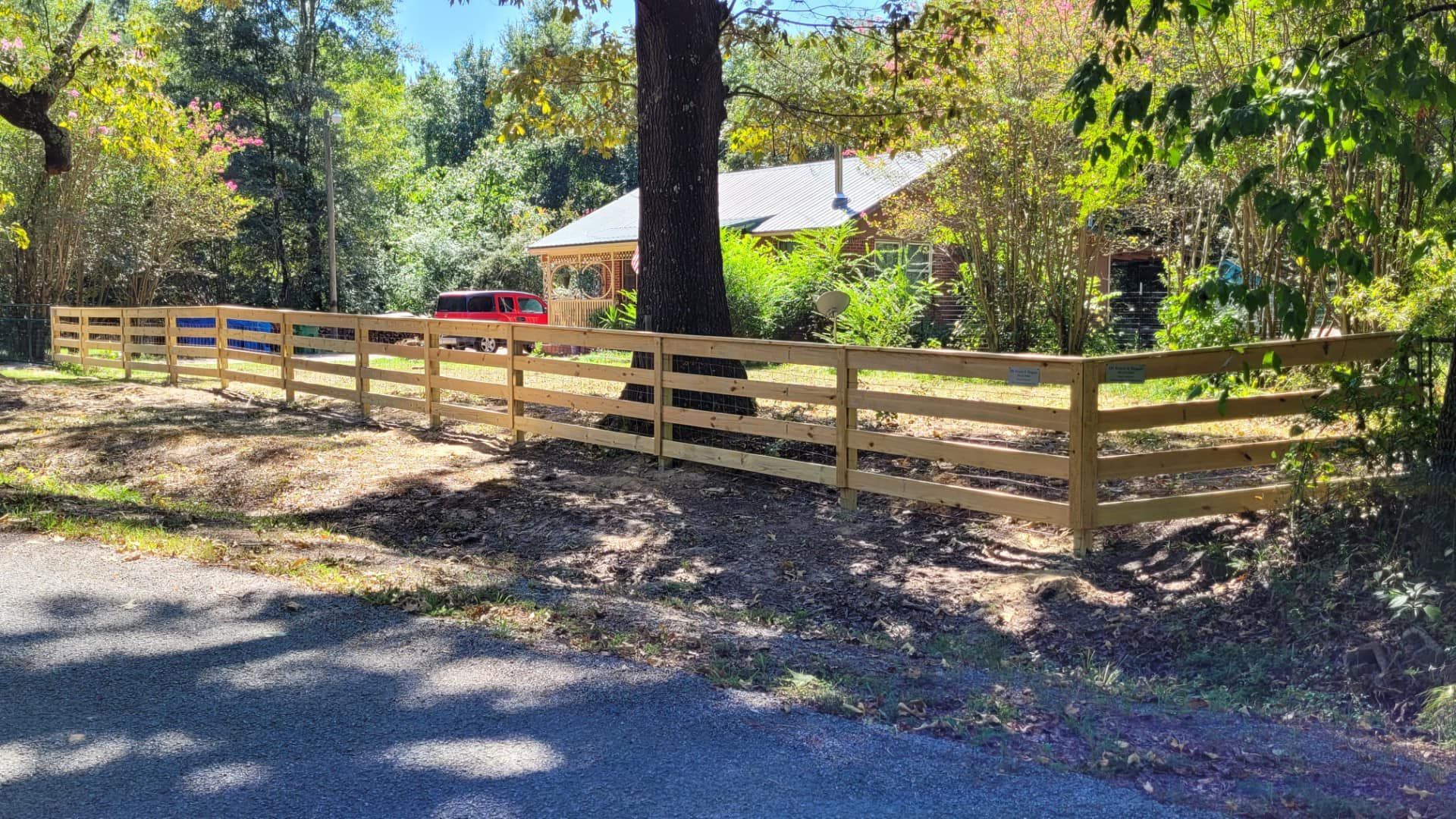 A wooden fence surrounds a dirt road in front of a house.