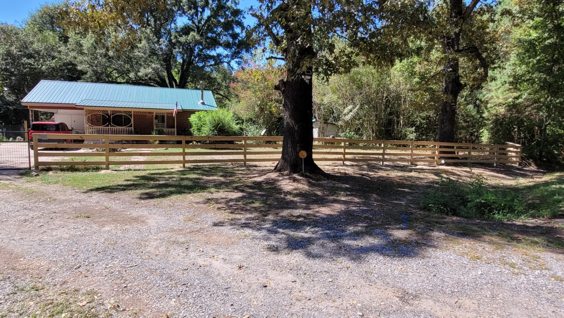 A wooden fence surrounds a house in the woods.
