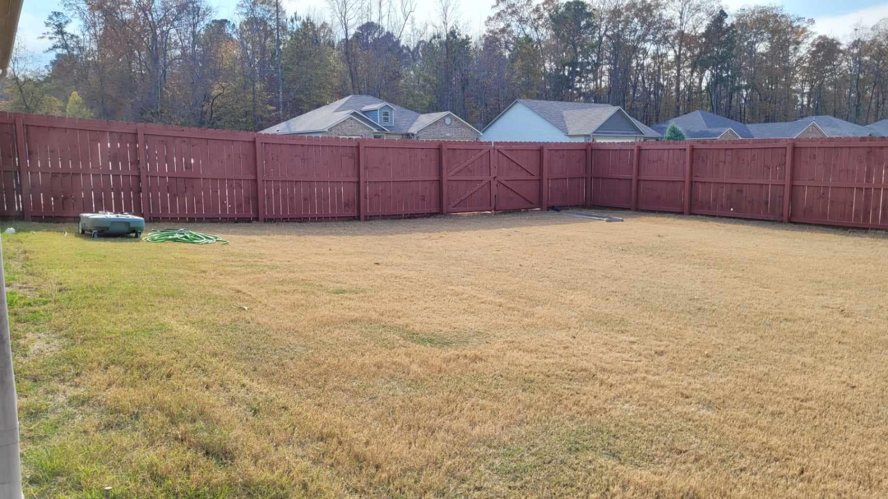 A wooden fence surrounds a large grassy field in a backyard.