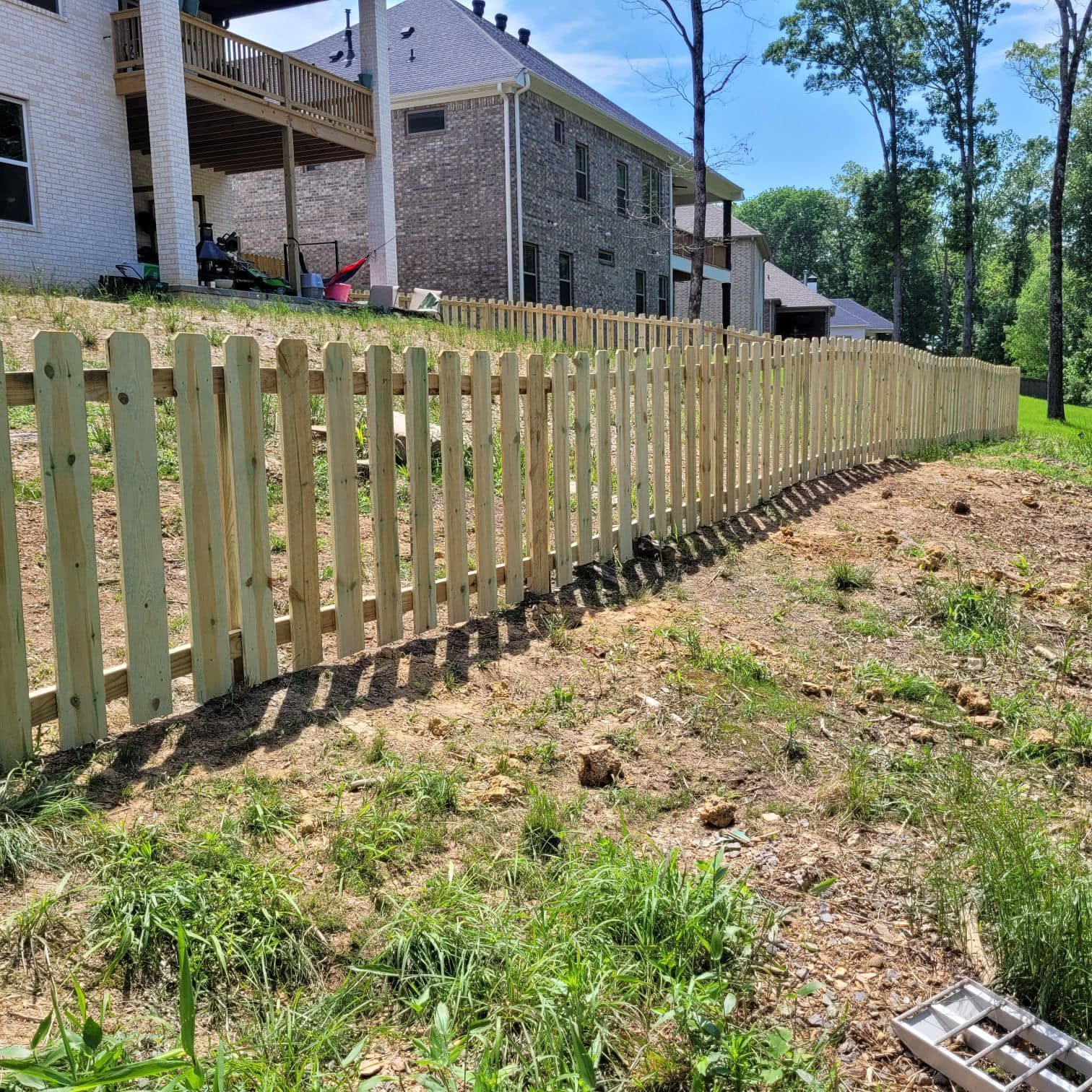 A wooden picket fence surrounds a grassy field in front of a house.