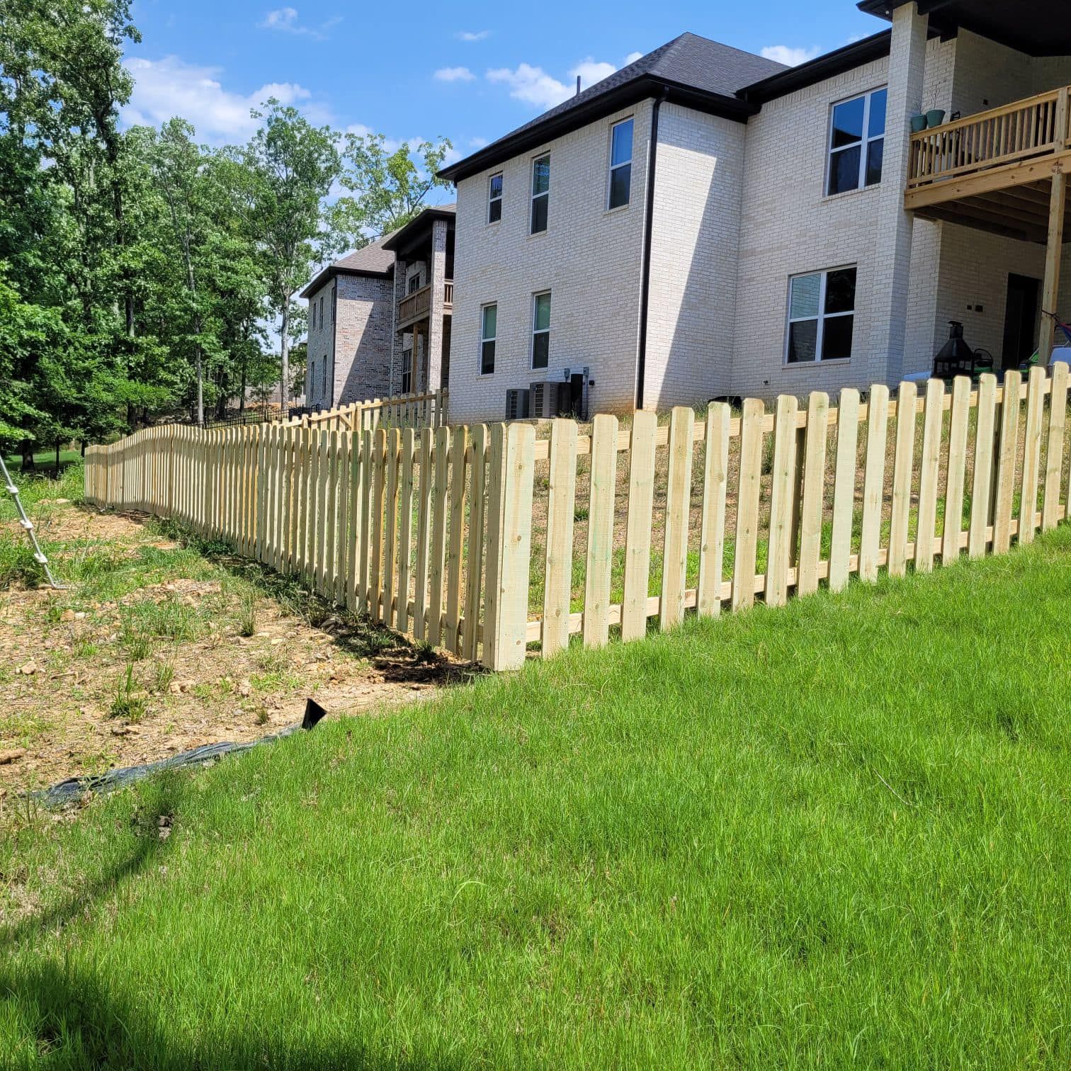 A wooden fence is sitting on top of a lush green hill in front of a house.