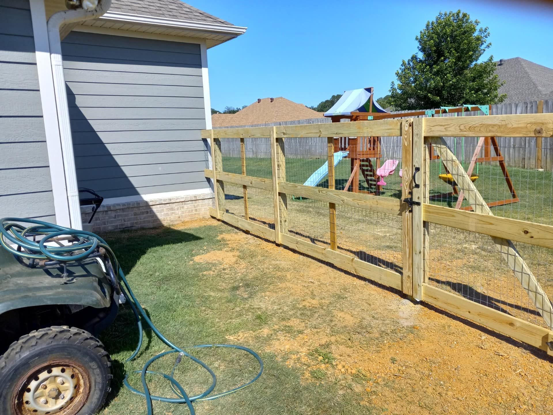 A wooden fence is being built in a backyard with a playground in the background.
