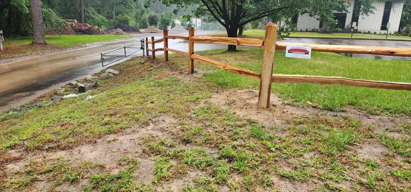 A wooden fence surrounds a grassy yard next to a dirt road.