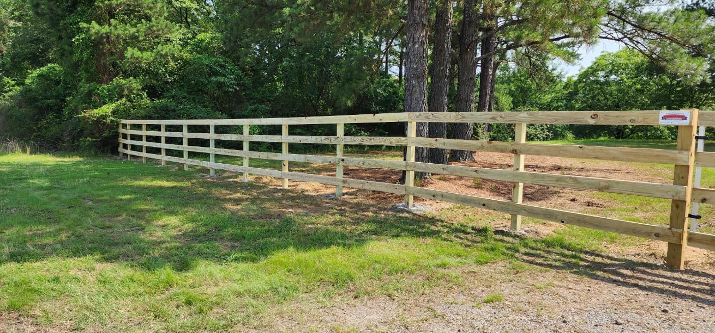 A wooden fence surrounds a grassy field with trees in the background.