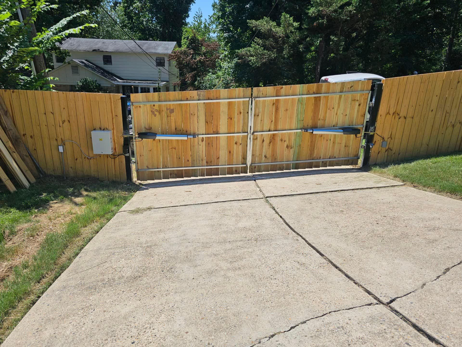A wooden fence with a gate in the middle of a driveway.