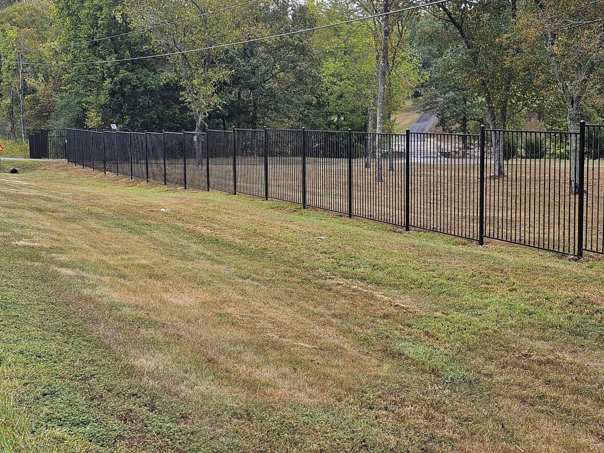 A metal fence surrounds a grassy field with trees in the background.