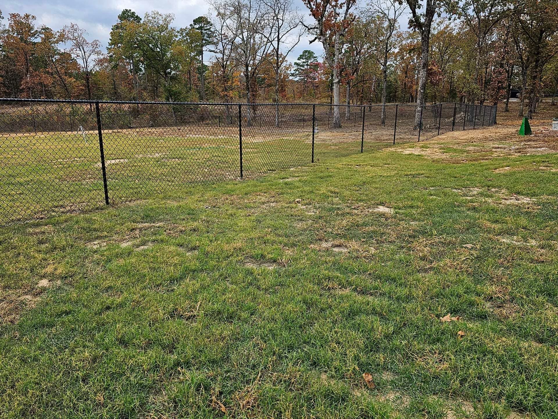 A large grassy field with a fence and trees in the background.