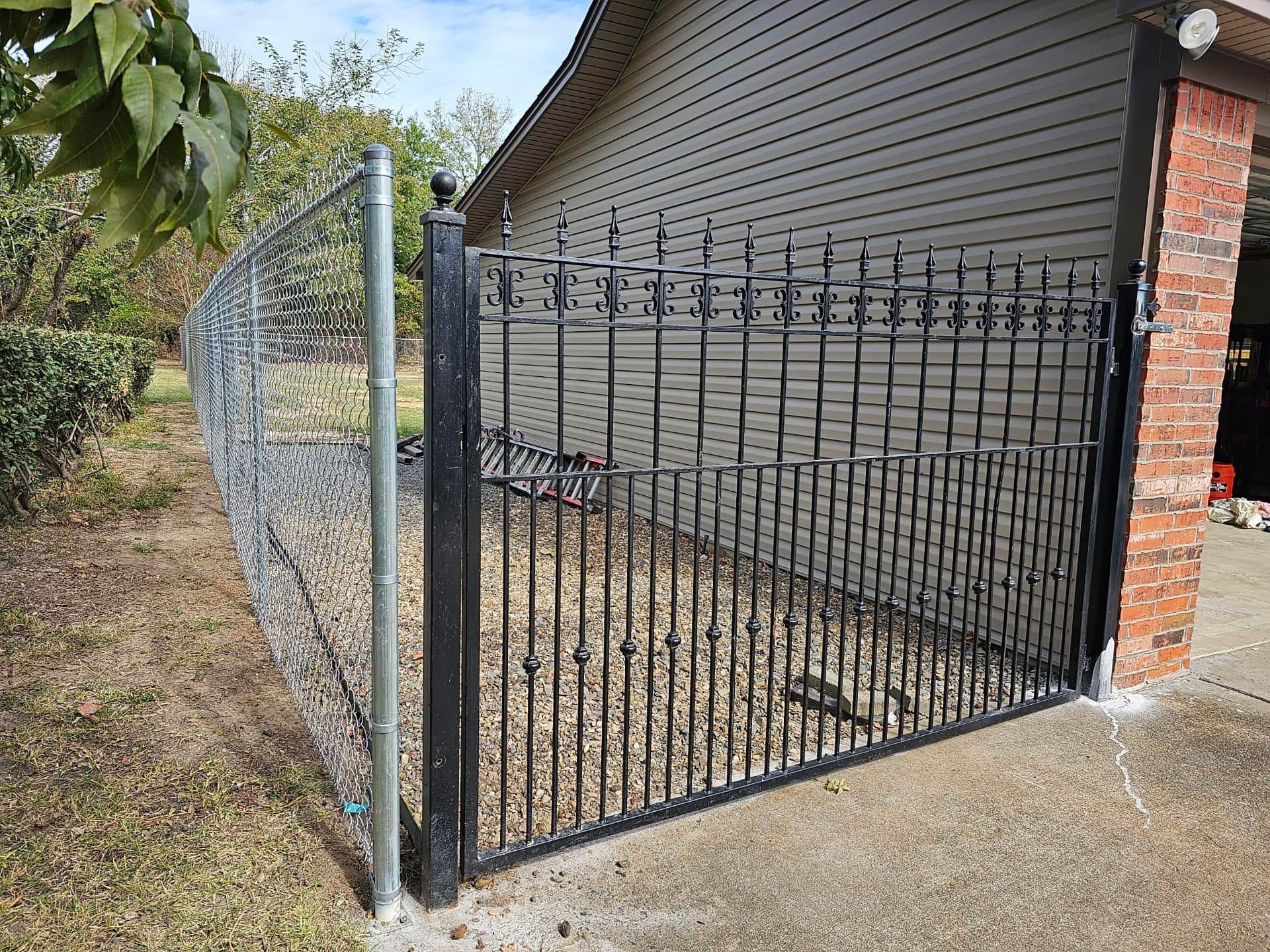 A wrought iron gate is sitting next to a chain link fence.