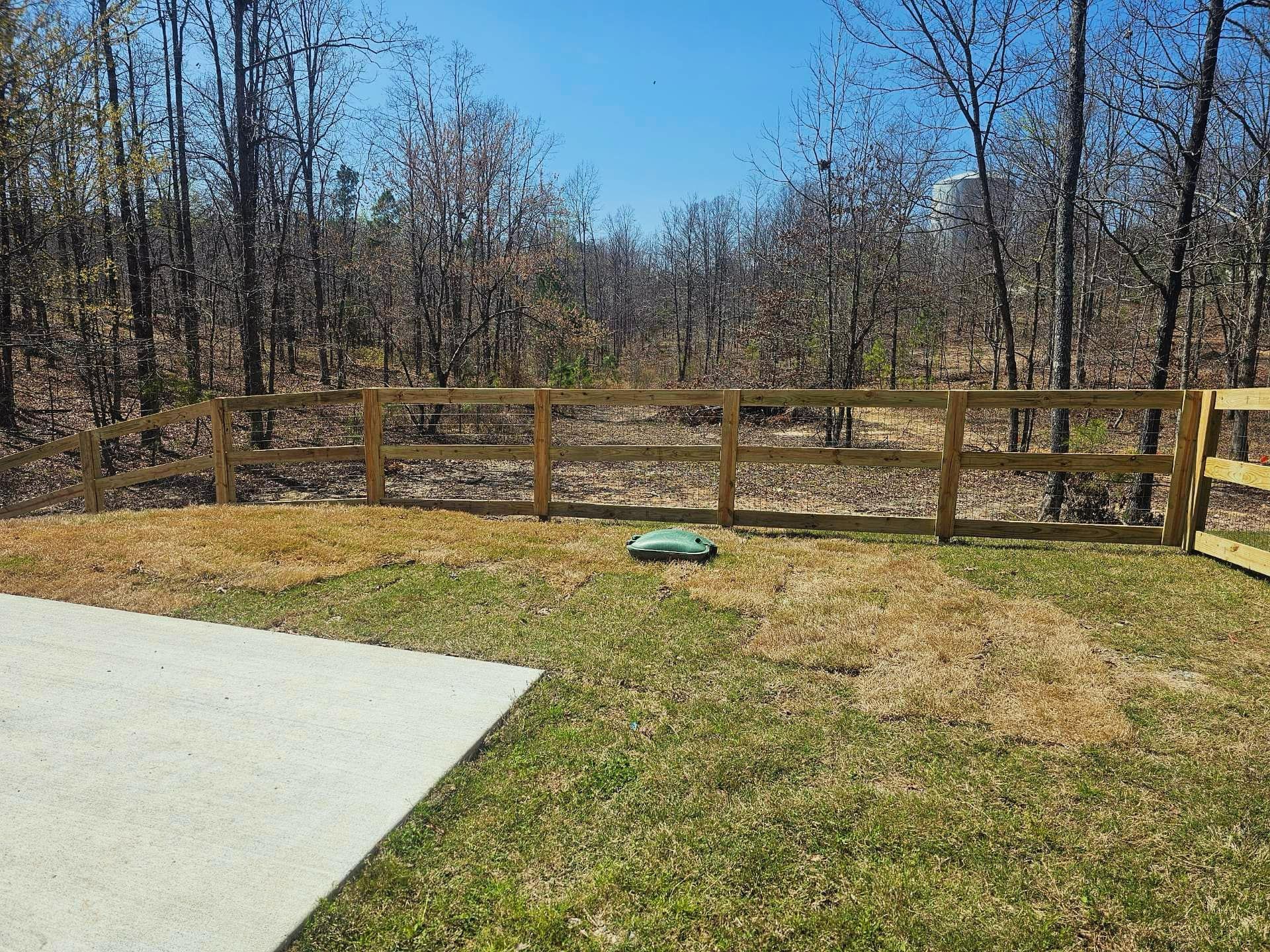 A wooden fence surrounds a lush green field with trees in the background.