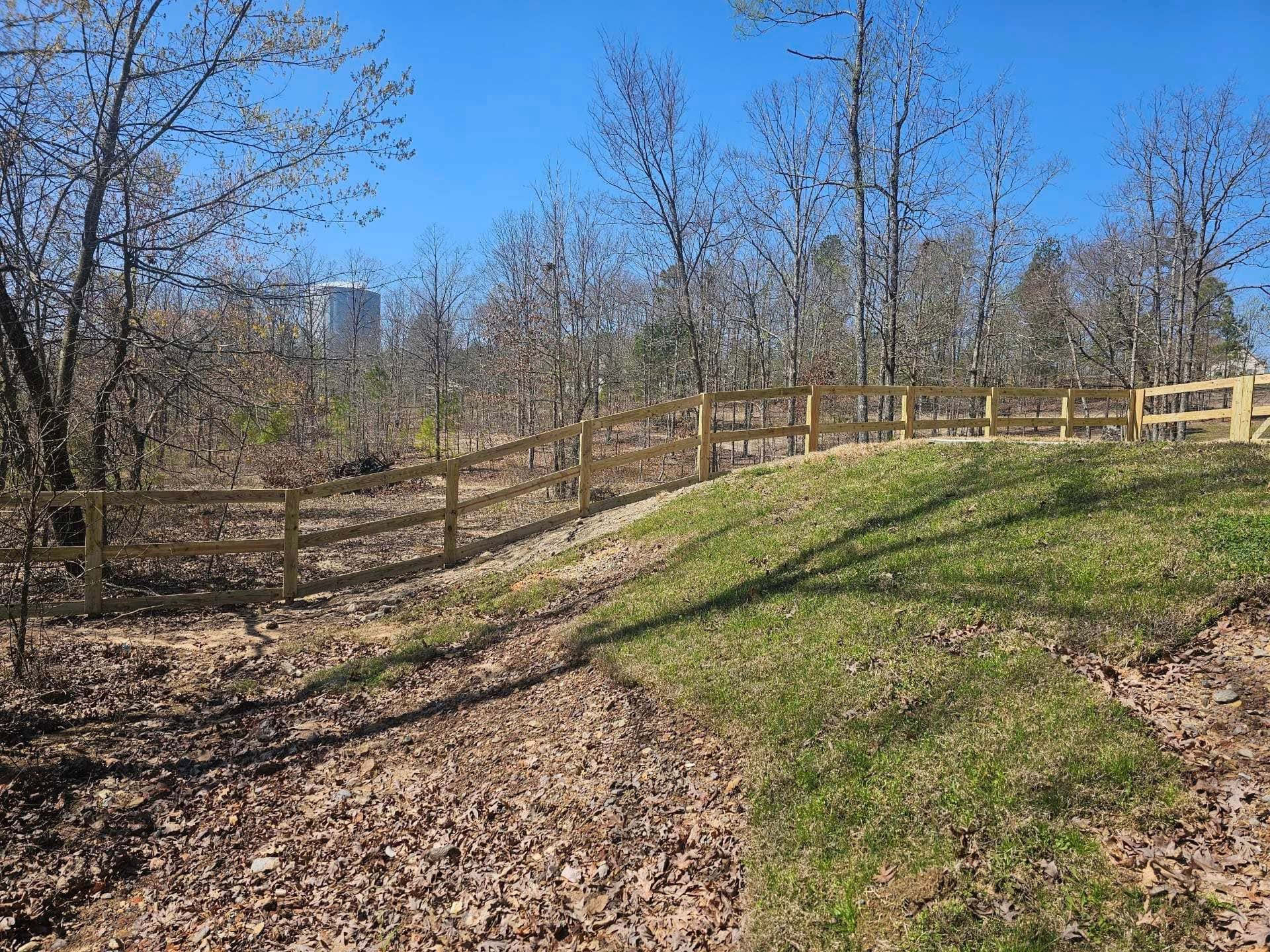 A wooden fence surrounds a grassy hill in the middle of a forest.