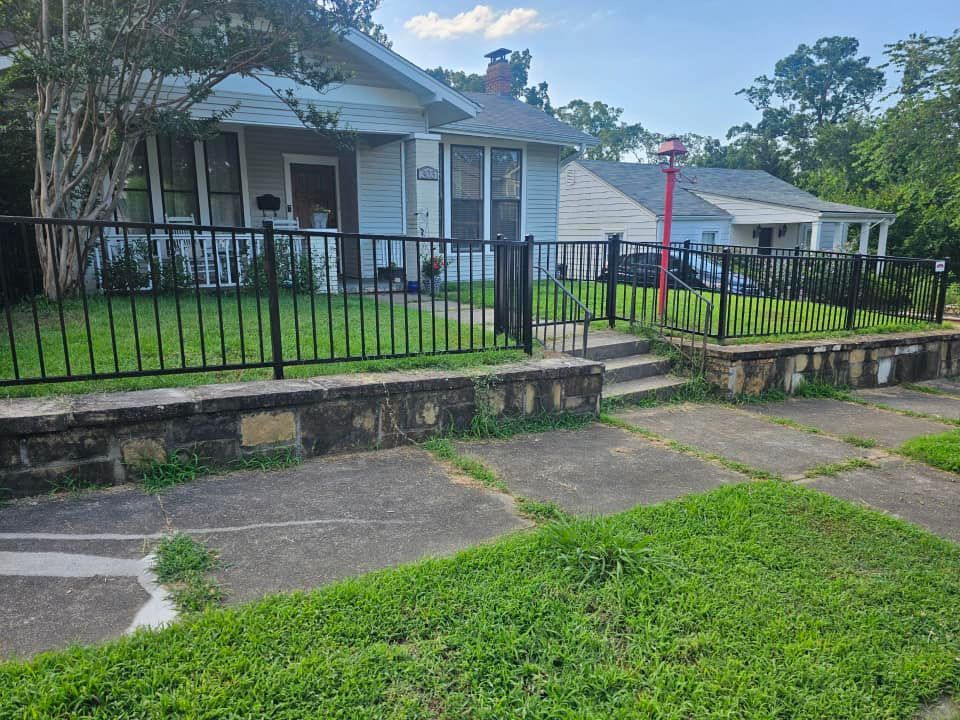 A house with a metal fence around it and a stone wall in front of it.