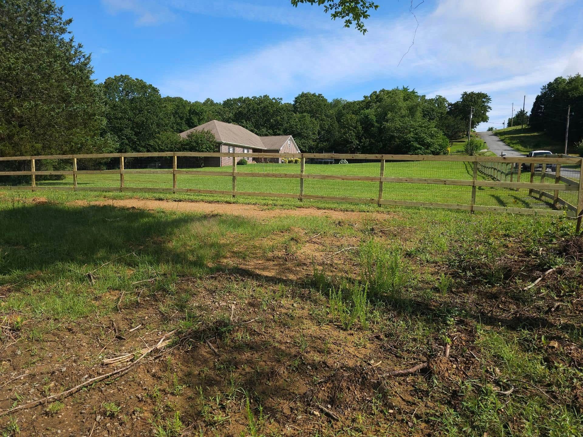A wooden fence surrounds a grassy field with a house in the background.