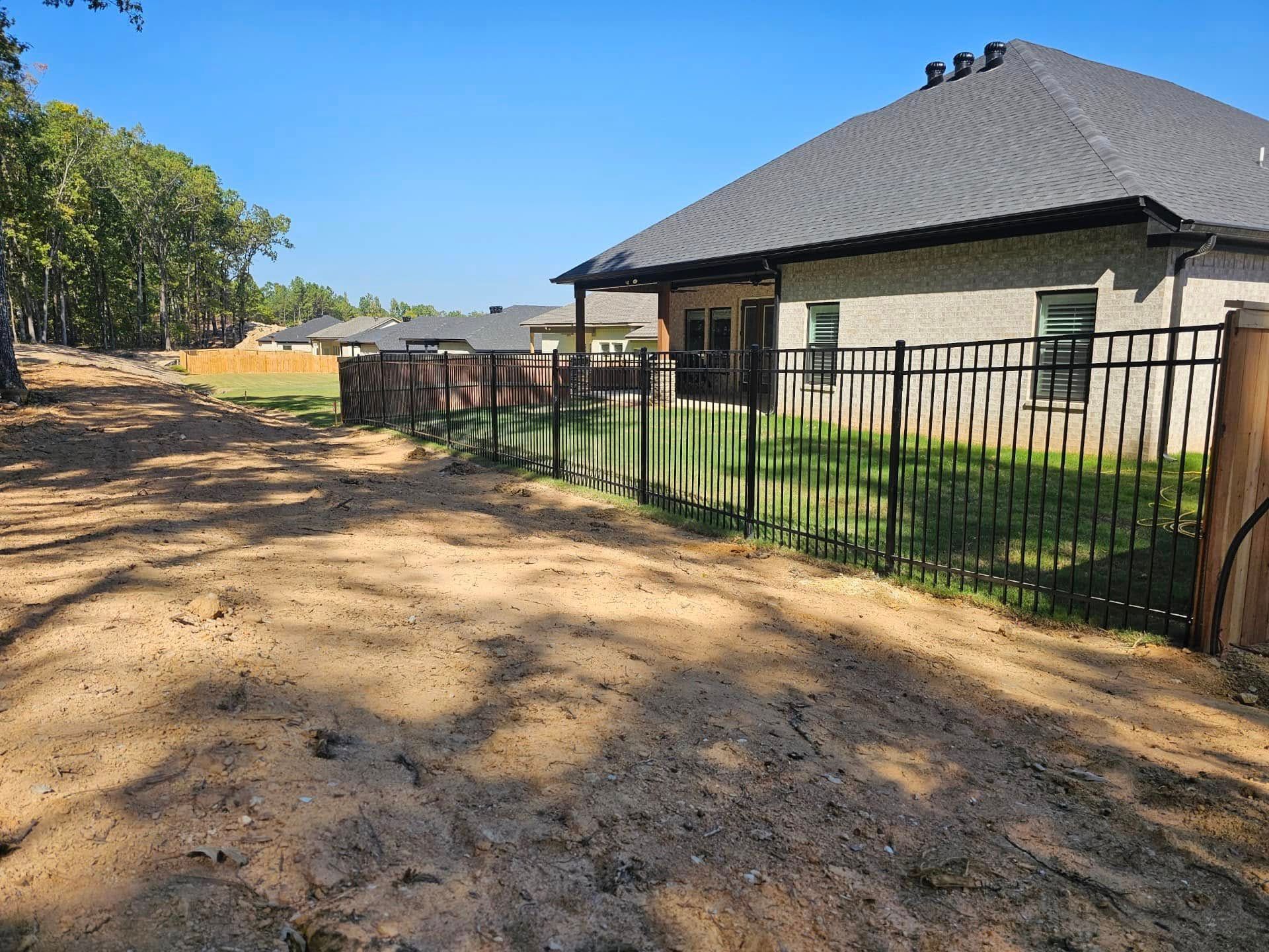 A house with a fence around it and a dirt road in front of it.