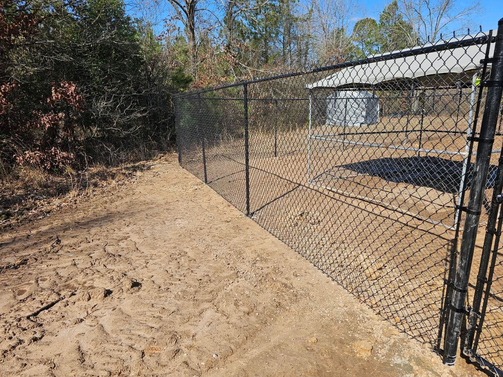A chain link fence surrounds a dirt path in a yard.