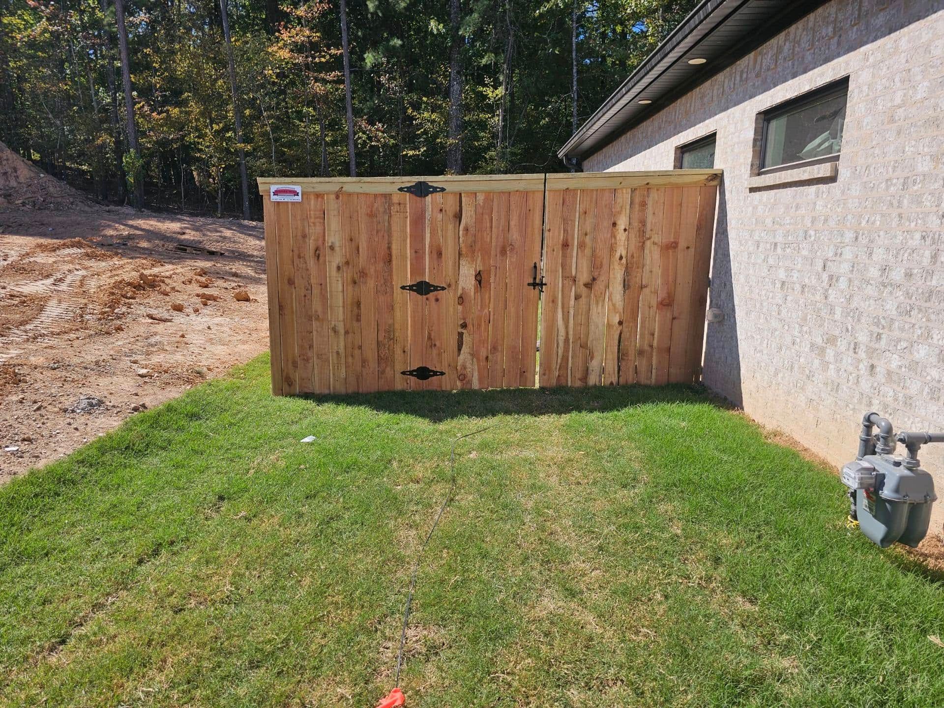 A wooden fence is sitting in the grass next to a house.