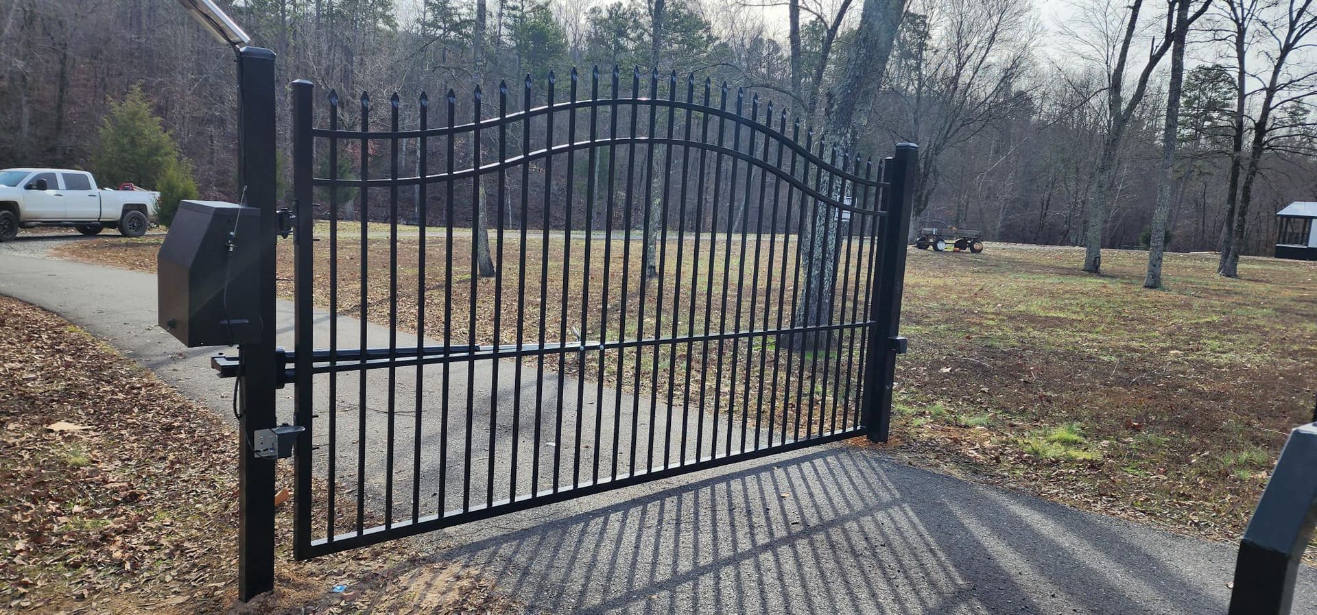 A black wrought iron gate is open to a driveway.