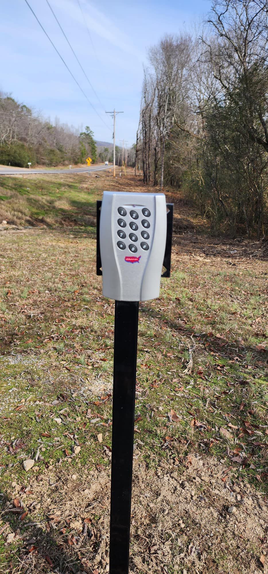 A keypad is sitting on top of a pole in a field.