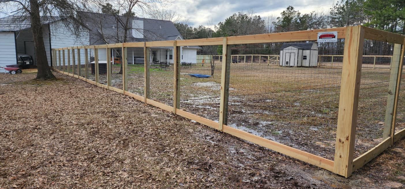 A wooden fence is surrounding a yard with a house in the background.