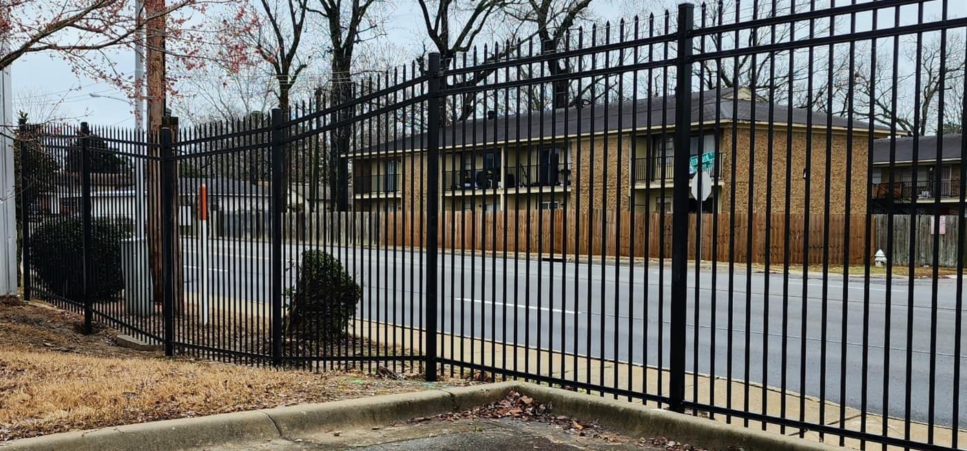 A black metal fence surrounds a parking lot in front of a building.