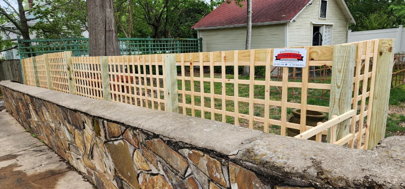 A wooden fence is sitting on top of a stone wall next to a house.