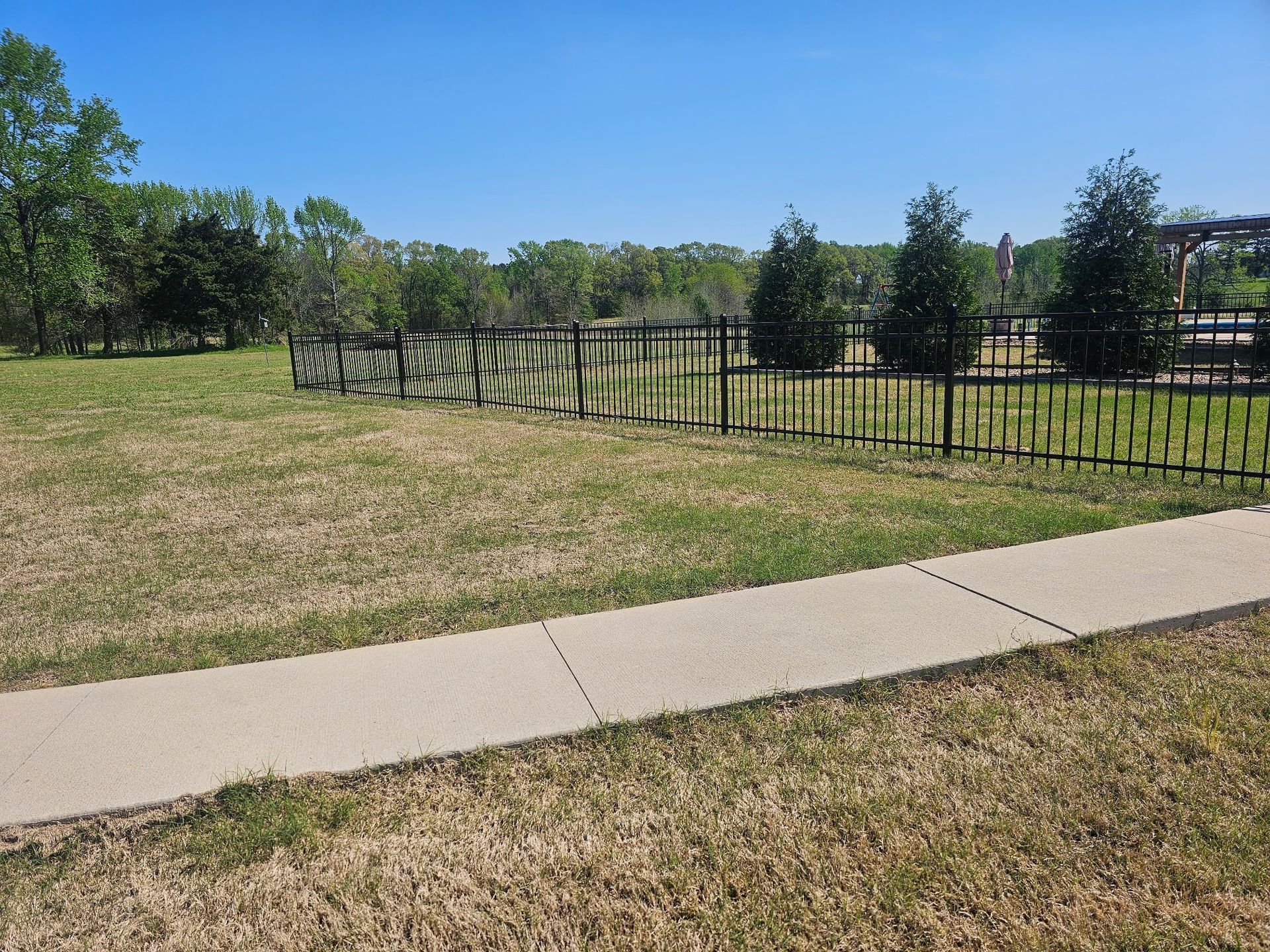 A sidewalk leading to a grassy field with a fence in the background.