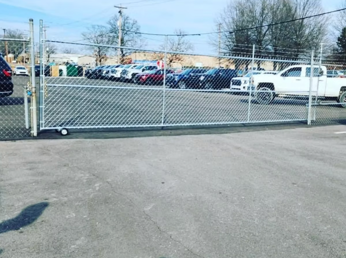 A white truck is parked behind a chain link fence in a parking lot.