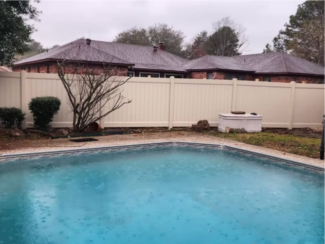 A large swimming pool with a white fence in the backyard of a house.