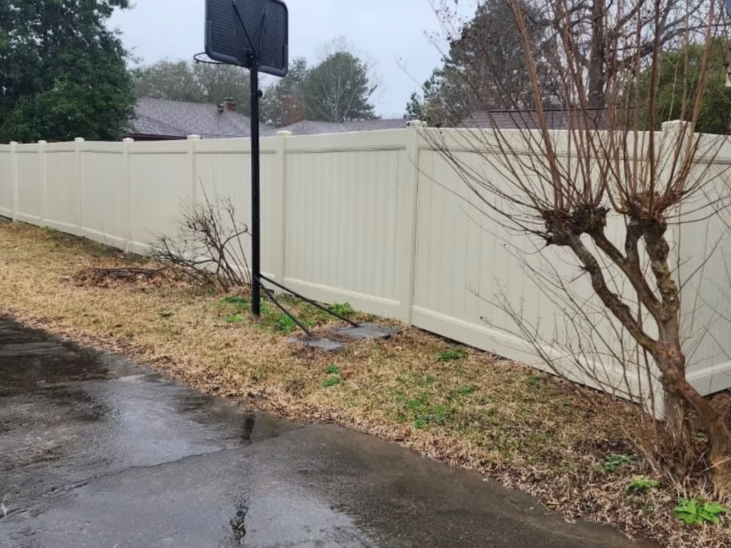 A white vinyl fence surrounds a yard with a basketball hoop in the background.