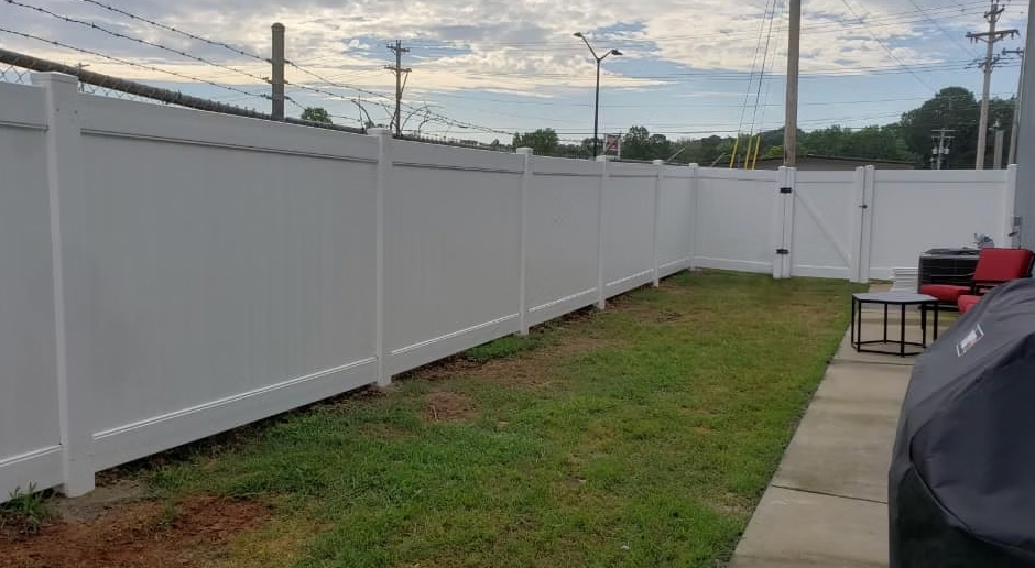 A white fence surrounds a lush green lawn in a backyard.