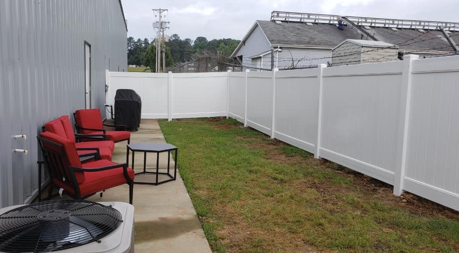 A backyard with a white fence , a couch , chairs and a table.