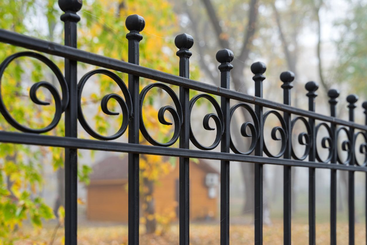 A close up of a wrought iron fence with trees in the background.