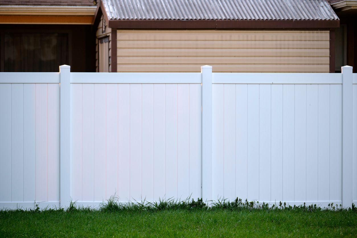 A white fence surrounds a lush green yard in front of a house.