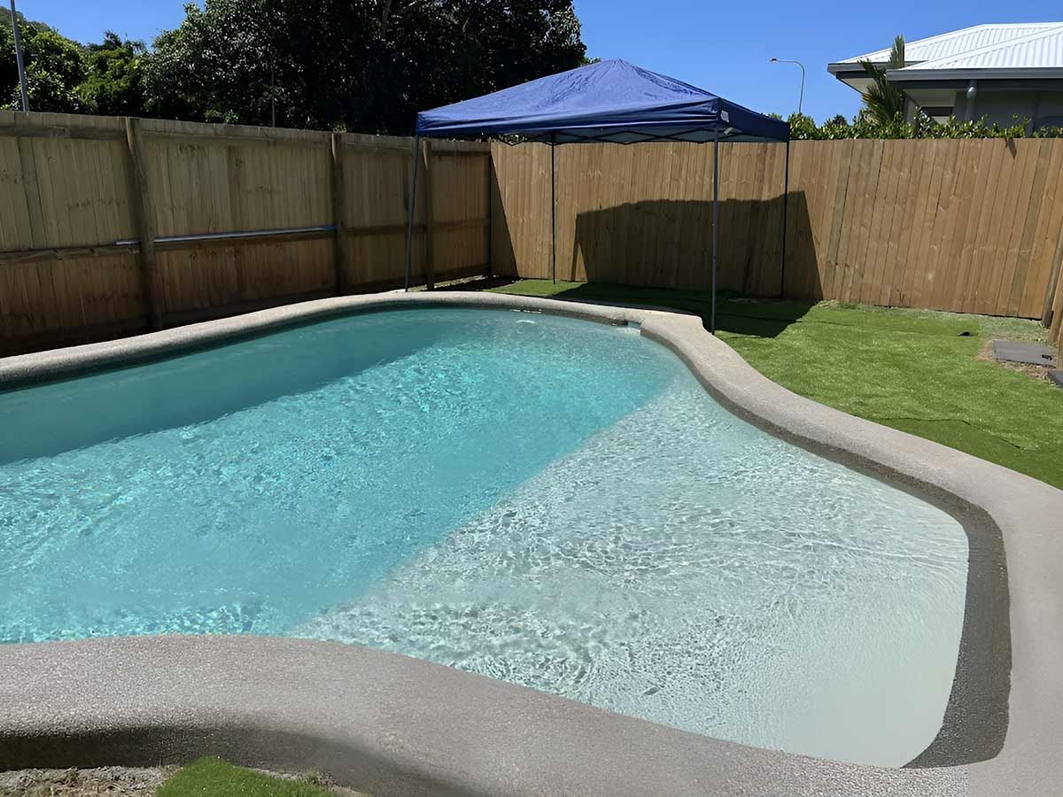 A Large Swimming Pool In A Backyard With A Wooden Fence — Pool Physicians NQ in Manoora, QLD