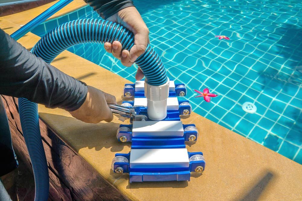A Person Is Cleaning A Swimming Pool With A Vacuum Cleaner — Pool Physicians NQ in Manoora, QLD