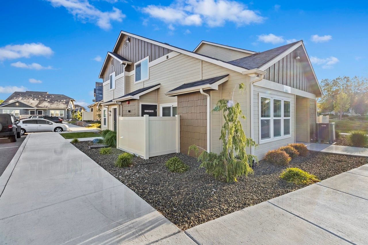 Exterior view of a modern multifamily building with a walkway, fence, and xeriscape landscaping.