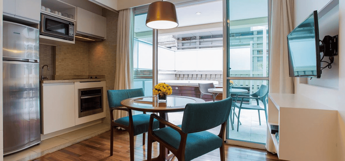 Cozinha e sala de jantar modernas com cadeiras azul-turquesa, mesa de madeira e porta de vidro deslizante para uma varanda.