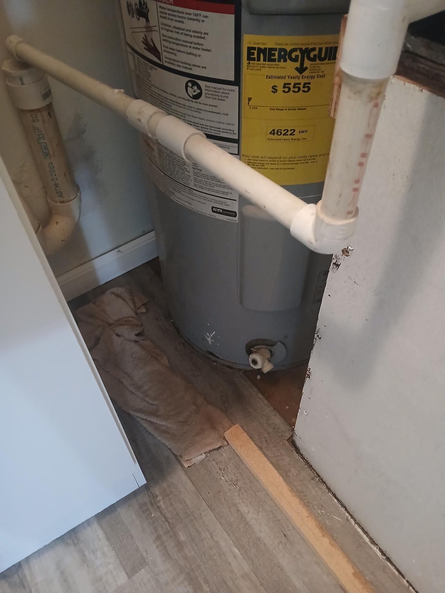 Water heater in a small space, with white pipes and a yellow energy label.