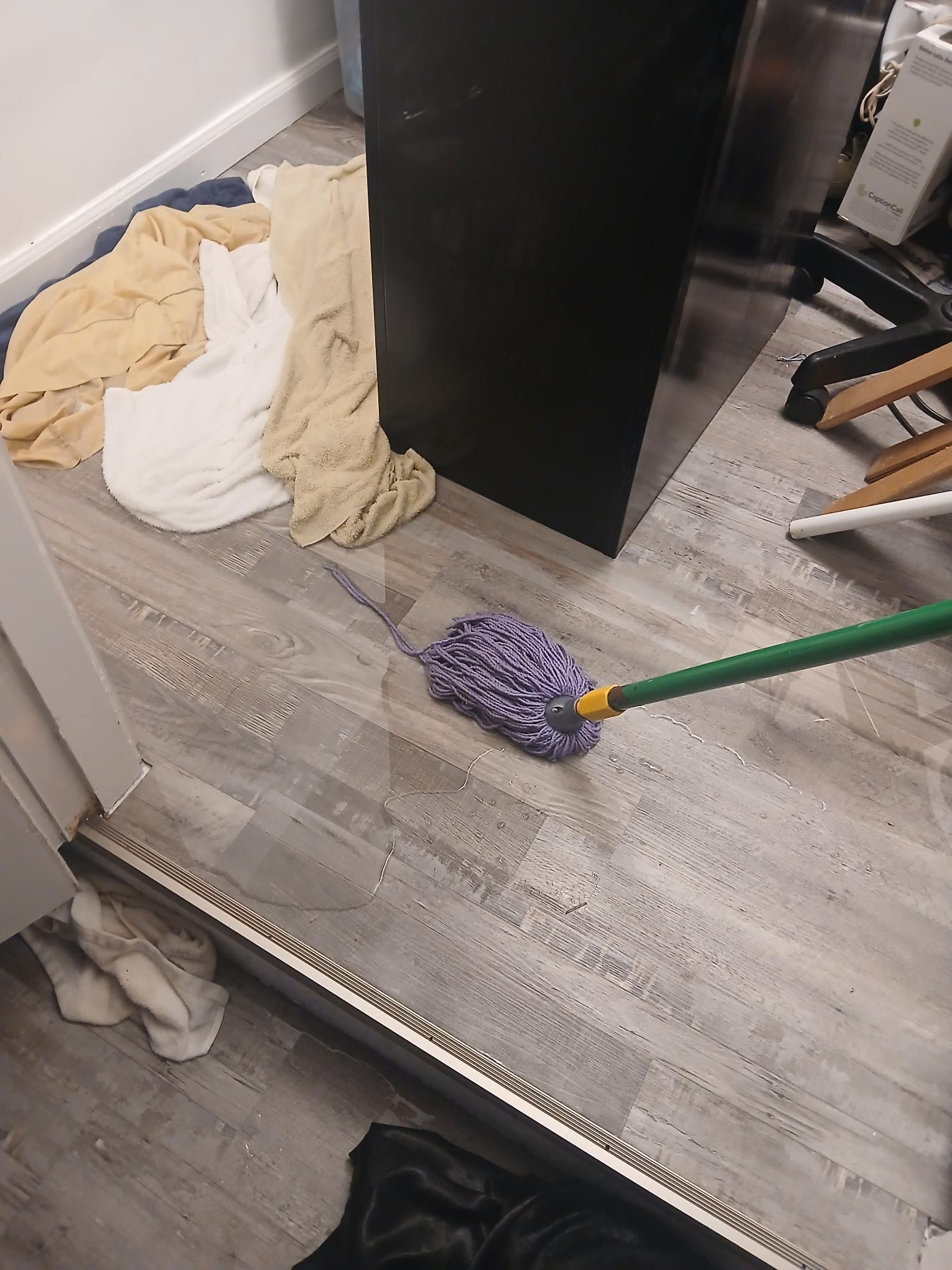 A person is mopping a gray floor; clothes are nearby. A black cabinet is in the background.