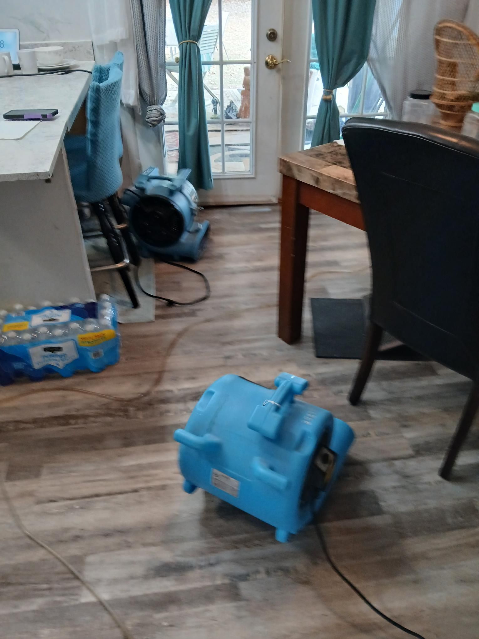 Two blue air movers on a wood floor near a door, likely drying after water damage.