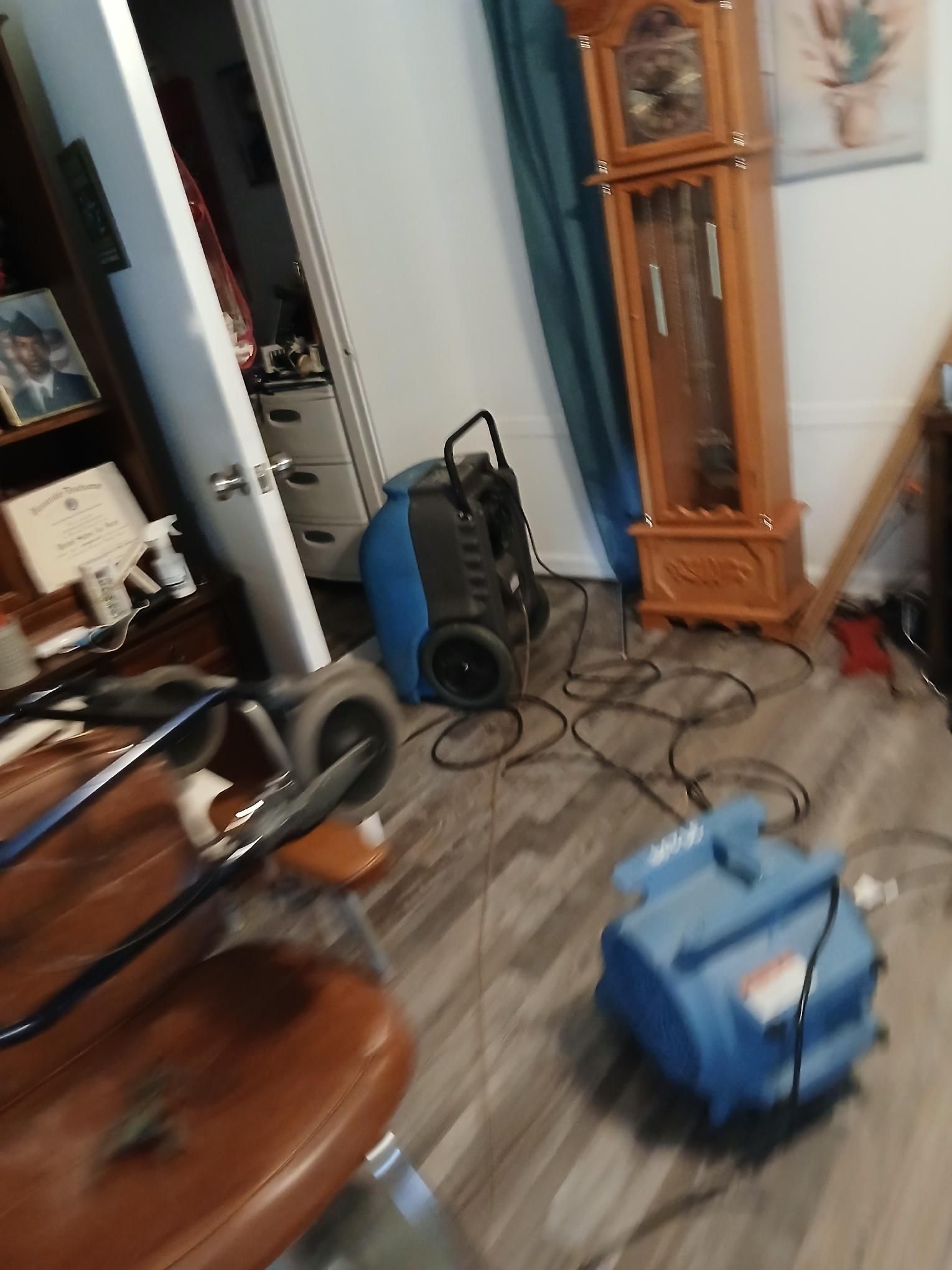 A blue dehumidifier and fan on a gray wood floor in a room with a grandfather clock.