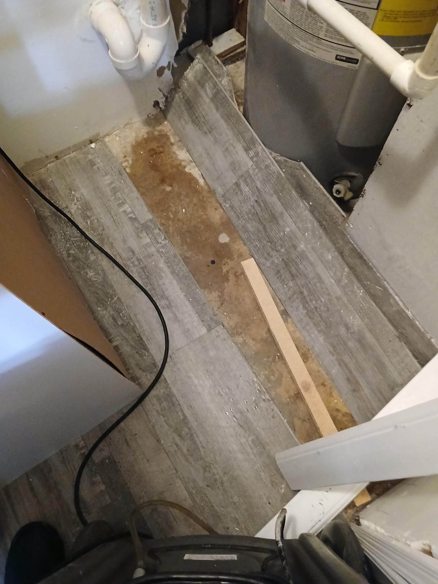 Water damaged floor next to a water heater. The floor is light grey, with brown discoloration.