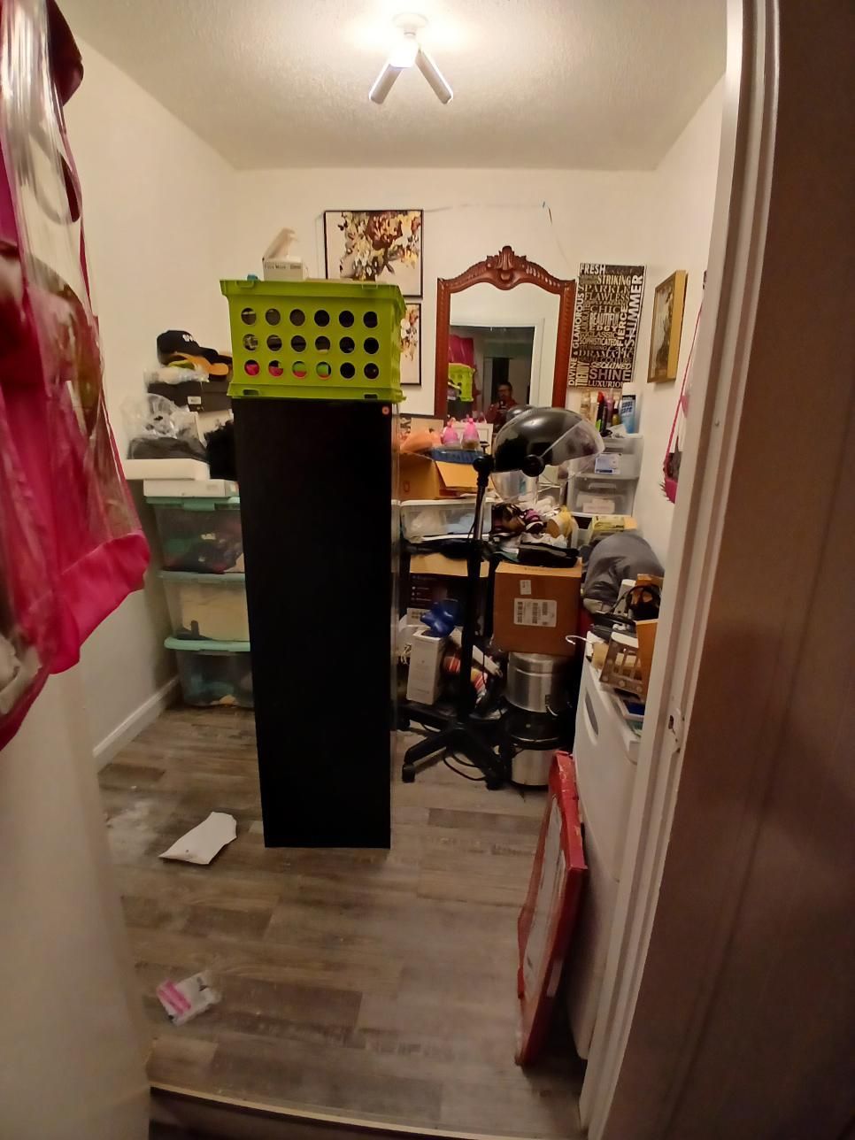 Cluttered small room with black cabinet, green basket, mirror, and various items on shelves.