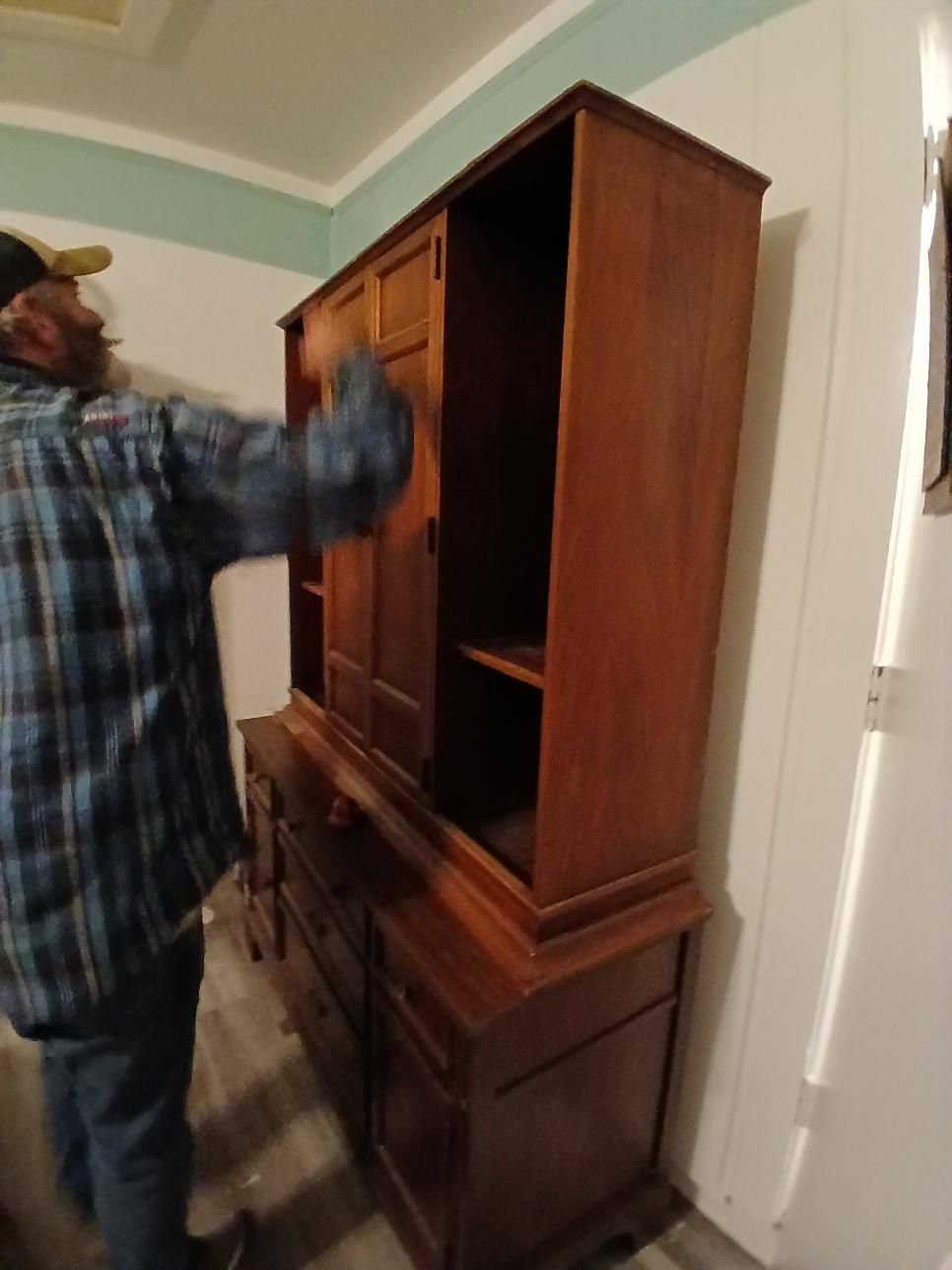 Man cleaning a large, dark wooden cabinet with open doors and drawers in a room.