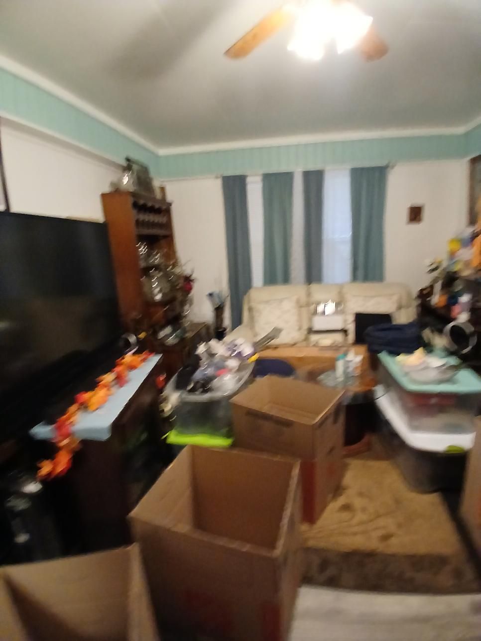 A cluttered living room with boxes, furniture, and objects scattered around.