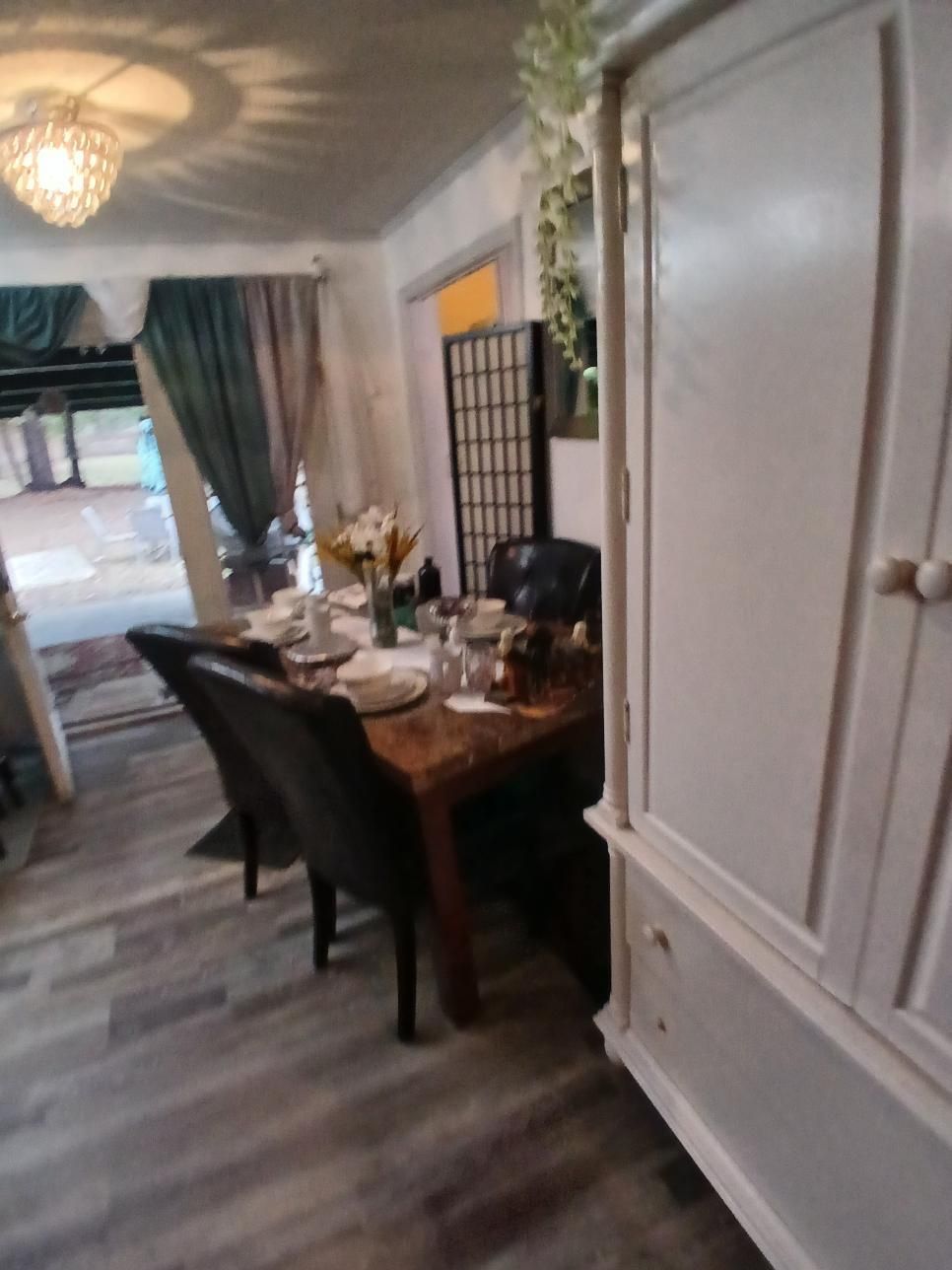 Dining room with table set for a meal. Black chairs, grey flooring, white armoire.